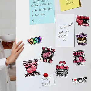 May include: A collection of colorful Bunco-themed magnets on a white refrigerator door. The magnets feature dice, hearts, and phrases like "Bunco Vibes," "Bunco Babe," and "What Happens at Bunco Stays at Bunco." There are also sticky notes.