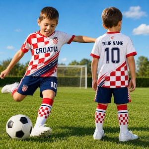 A young boy in a Croatia soccer uniform is playing with a soccer ball on a grassy field.