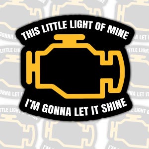 May include: A black sticker featuring a yellow engine symbol with the text "THIS LITTLE LIGHT OF MINE" above and "I'M GONNA LET IT SHINE" below. The sticker has a white border.
