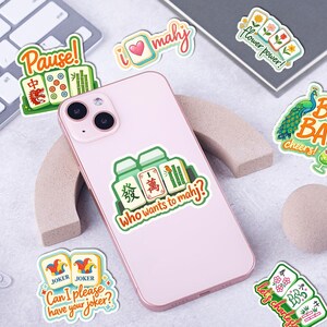 a pink smartphone with various stickers on it, including one with a joker and another with a flower.