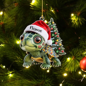 May include: A Christmas ornament featuring a cartoon turtle wearing a Santa hat with the word "Name" on it. The turtle has a green shell and is decorated with Christmas lights. A small Christmas tree is behind the turtle.