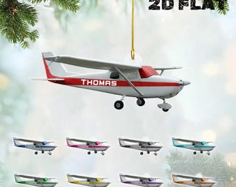 May include: A white and red airplane ornament with the name "THOMAS" on the side. The ornament is hanging from a gold string. Below are several smaller airplane ornaments in various colors, including blue, pink, and green. The text "2D FLAT" is at the top.
