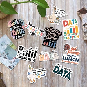 Puede incluir: Una colecci&oacute;n de pegatinas coloridas con frases y gr&aacute;ficos relacionados con datos. Las pegatinas presentan frases como "Collecting Data is my Cardio" y "Show me the Data". Las pegatinas est&aacute;n sobre una superficie de madera.