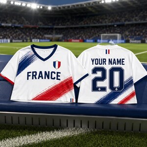 A white soccer jersey with red and blue stripes, featuring the word "FRANCE" and the number 20, is displayed on a bench in a stadium.