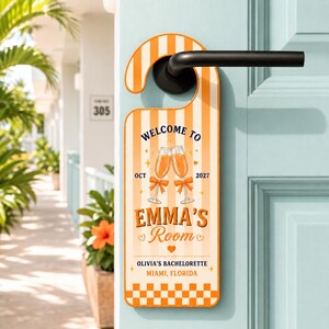 May include: A vertical door hanger with orange and white vertical stripes, featuring two champagne glasses with orange bows, the text WELCOME TO EMMA'S ROOM, OCT 2027, OLIVIA'S BACHELORETTE, and MIAMI, FLORIDA, with a checkered pattern at the bottom edge.