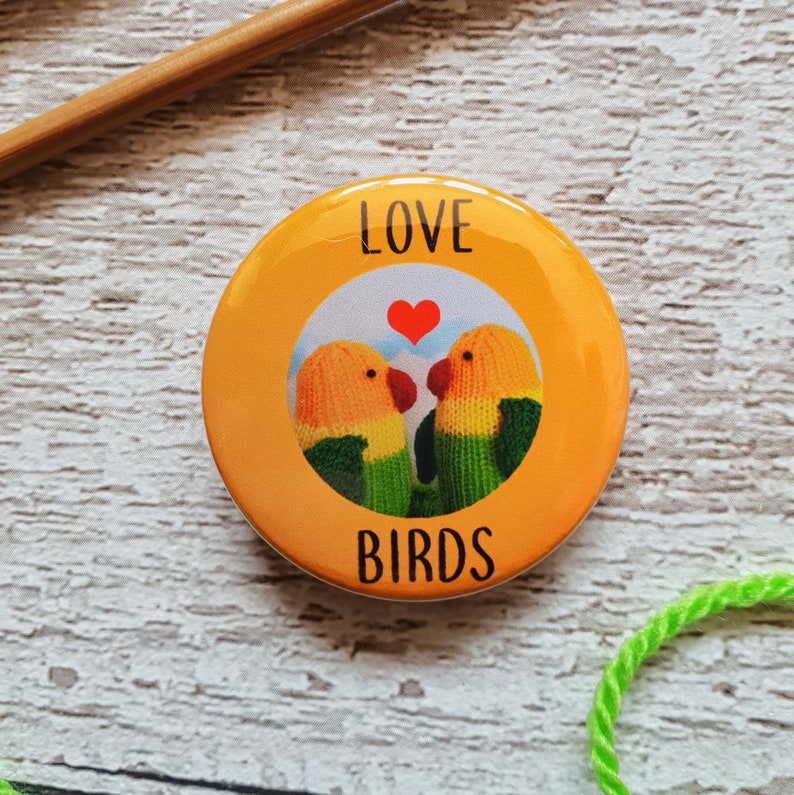 An orange button badge with a photo of knitted lovebirds on it and the text Love Birds.