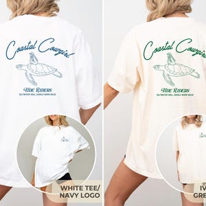 May include: Two oversized t-shirts with a graphic of a sea turtle and the text "Coastal Cowgirl" and "Tide Riders" on the back. The shirt on the left is white with a navy blue graphic and the shirt on the right is ivory with a green graphic.