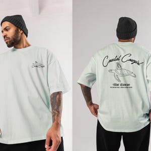 May include: A light blue t-shirt with a graphic of a sea turtle and the text "Coastal Cowgirl Tide Riders Saltwater Soul, Saddle Worn Sole" printed on the front.