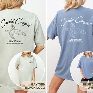 May include: Two oversized t-shirts with a graphic of a sea turtle and the text "Coastal Cowgirl" and "Tide Riders" on the back. The left shirt is a light blue color with a black logo. The right shirt is a light green color with a white logo.