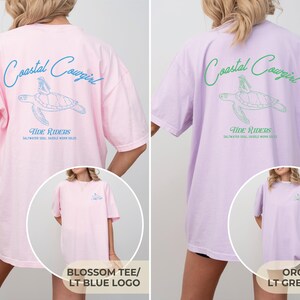 May include: Two oversized t-shirts with a sea turtle graphic and the text "Coastal Cowgirl" and "Tide Riders" printed on the back. The left shirt is pink with a light blue graphic and the right shirt is lavender with a light green graphic.