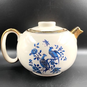 May include: White teapot with a gold trim and a blue and white floral design featuring birds.