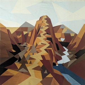May include: A fabric quilt wall hanging featuring a geometric mountain landscape. The design uses angular patches of brown, tan, ochre, and black fabric to depict a central peak and rocky terrain, with a light blue sky and a blue river flowing below.