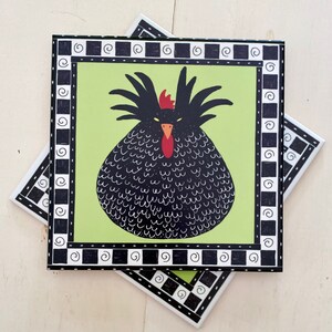 May include: Square ceramic tile featuring a whimsical illustration of a black chicken with a red comb and beak, set against a light green background. The tile is framed with a black and white border. Additional tiles are visible.