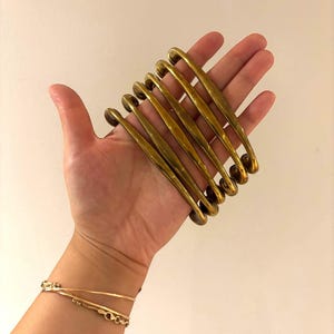 May include: A set of six curved, polished brass drawer pulls with a smooth, rounded finish. Each handle features a long, slender arch shape with circular mounting points at both ends, showcasing a warm, metallic gold-toned surface texture.