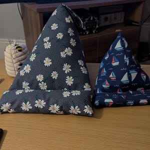 May include: Two triangular reading pillows, one with a white daisy pattern on a dark blue background and the other with a blue and red sailboat pattern on a dark blue background.