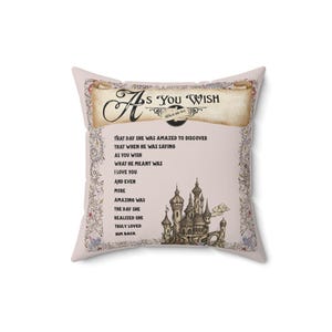 Puede incluir: Un cojín cuadrado decorativo con el texto "As You Wish" en un diseño de pergamino. El cojín presenta un fondo rosa claro con una ilustración de castillo y texto romántico.