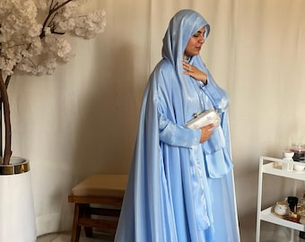 May include: A light blue prayer robe with a hood and a white clutch purse. The robe is made of a silky material and has a flowing design.