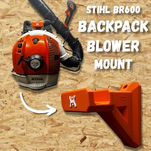 May include: An orange STIHL BR600 backpack blower and its matching orange mount are displayed against a wood-grain background. The blower is black, orange, and white. The mount has a white logo. Text on the image reads "STIHL BR600 BACKPACK BLOWER MOUNT."
