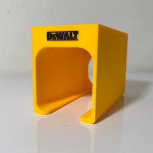 May include: A yellow plastic tool holder with the word "DEWALT" printed on the front. The holder has a slot for holding a tool.