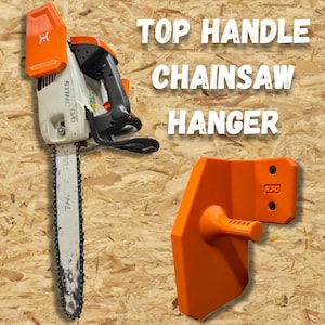 May include: A white and orange chainsaw with a black handle and a matching orange top handle chainsaw hanger. The text "TOP HANDLE CHAINSAW HANGER" is displayed in white block letters.