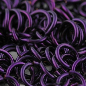 May include: Close-up of a chainmail mesh made of small, interconnected metal rings. The rings are a deep purple color, creating a rich and textured appearance.