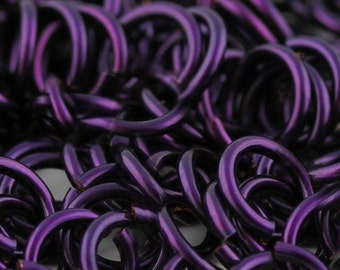 May include: Close-up of a chainmail mesh made of small, interconnected metal rings. The rings are a deep purple color, creating a rich and textured appearance.