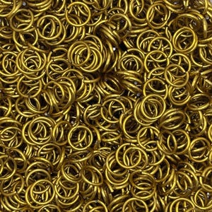 Puede incluir: Una gran colecci&oacute;n de peque&ntilde;os anillos de salto met&aacute;licos circulares de color dorado. Cada anillo es uniforme en forma y tama&ntilde;o, con un acabado liso y pulido. Los anillos est&aacute;n densamente agrupados, creando una superficie met&aacute;lica texturizada.