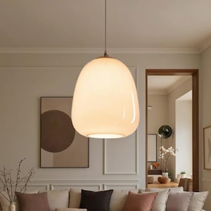 Könnte beinhalten: Eine große, eiförmige Pendelleuchte mit einem warmen, weiß leuchtenden Schirm. Das Licht hängt an einem dünnen, braunen Kabel. Die Leuchte ist ein modernes Designelement für die Innenbeleuchtung.