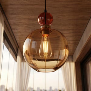 Puede incluir: Una lámpara colgante con una gran pantalla de vidrio ámbar de forma redonda. La bombilla interior es una bombilla Edison de estilo vintage. La lámpara tiene una parte superior de color rojo oscuro y una base de color latón.