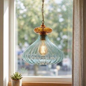 May include: A teal glass pendant light with a gold-coloured top, suspended from a gold chain. The light bulb is visible inside the shade. The background includes a window and a curtain. The light fixture is a decorative element.