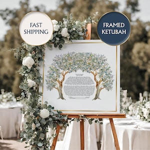 May include: A framed Ketubah, a Jewish marriage contract, displayed on an easel. The artwork features two stylized trees with olive branches, surrounding the text of the Ketubah. The frame is gold, and the background is a blurred outdoor scene.