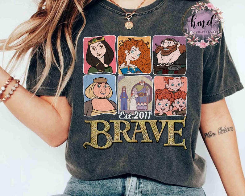 May include: Dark gray t-shirt featuring a graphic of characters from the animated film "Brave." The design includes six framed images of characters, the text "Est. 2011," and the word "BRAVE" in gold lettering.