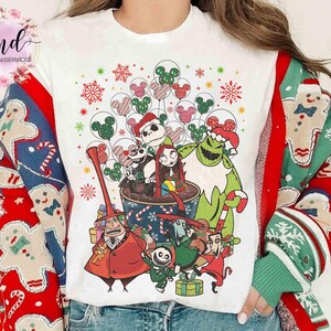 May include: A white t-shirt featuring a graphic print of characters from The Nightmare Before Christmas, including Jack Skellington, Sally, and Oogie Boogie, surrounded by festive holiday elements like snowflakes and Mickey Mouse balloons.