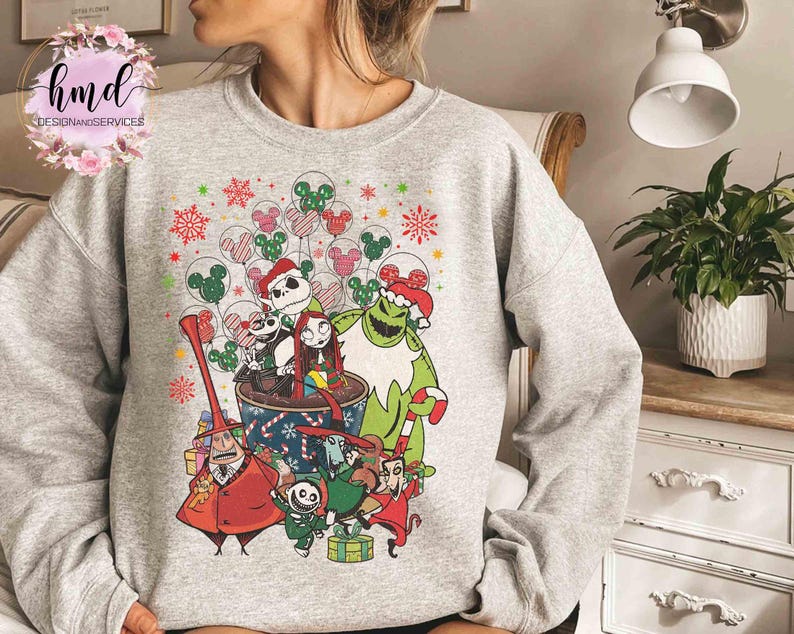 May include: A light gray crewneck sweatshirt featuring a colorful graphic print of characters from The Nightmare Before Christmas, including Jack Skellington and Sally, surrounded by festive holiday balloons and candy cane patterns.