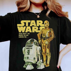 Könnte beinhalten: Schwarzes T-Shirt mit gelbem Star Wars-Logo und dem Text "These aren't the droids you are looking for...". Das Design zeigt Bilder von C-3PO und R2-D2 im Vintage-Stil.
