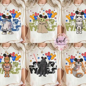 May include: Cream-colored t-shirts featuring Star Wars characters with Mickey Mouse ears and balloons. Designs include R2-D2, Grogu, a Stormtrooper, C-3PO, Darth Vader, and BB-8. The word "STAR WARS" is printed on each shirt.