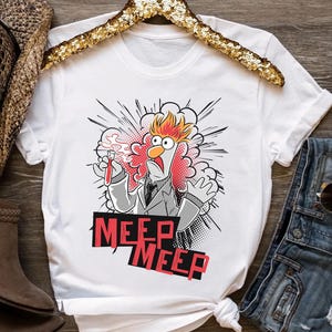 May include: White t-shirt featuring a cartoon character with orange hair and a lab coat, holding a test tube. The shirt has the text "MEEP MEEP" in red and black. The design is in a comic book style.