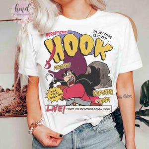 May include: A white t-shirt featuring a graphic of Captain Hook with a purple hat and red coat. The text reads: HORRIFYING! PLAYTIME IS OVER... HOOK PIRATES! TICK TOCK! TIMES UP! CAPTAIN OF BAD! LIVE! FROM THE INFAMOUS SKULL ROCK in yellow, red, and black.