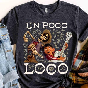 Peut inclure: T-shirt gris fonc&eacute; avec un graphisme color&eacute; du film Disney Coco. Le motif comprend un personnage squelette, un gar&ccedil;on jouant de la guitare et les mots "UN POCO LOCO" en blanc. Le t-shirt est &agrave; col rond.