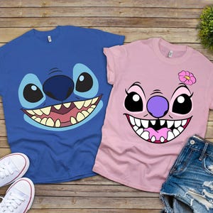 May include: Two t-shirts featuring cartoon character faces. One is blue with a large, smiling face, and the other is pink with a similar design and a flower. White sneakers and denim shorts are also visible.