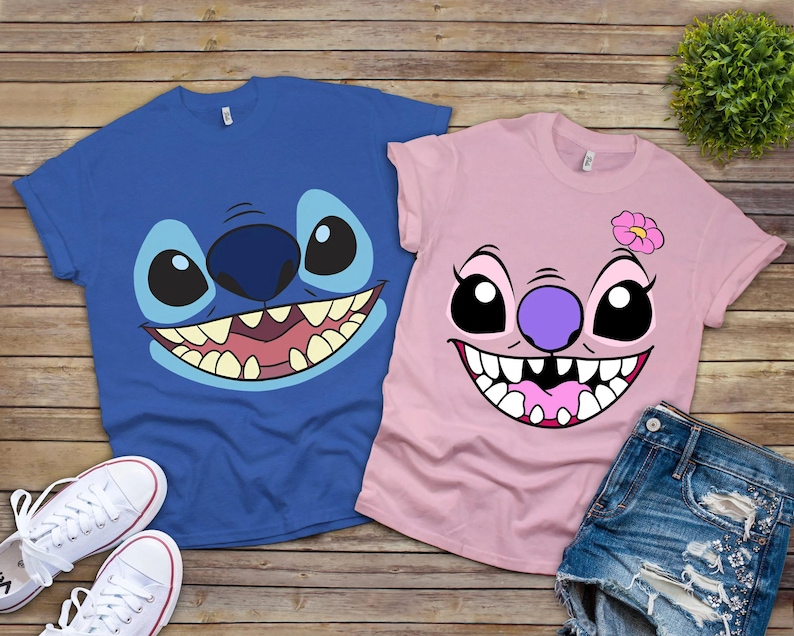 May include: Two t-shirts featuring cartoon character faces. One is blue with a large, smiling face, and the other is pink with a similar design and a flower. White sneakers and denim shorts are also visible.