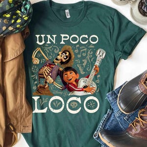 Peut inclure: T-shirt vert fonc&eacute; avec un motif du film Coco. Le design comprend un squelette, un gar&ccedil;on jouant de la guitare et les mots "UN POCO LOCO". Des notes de musique et des &eacute;l&eacute;ments d&eacute;coratifs entourent les personnages.