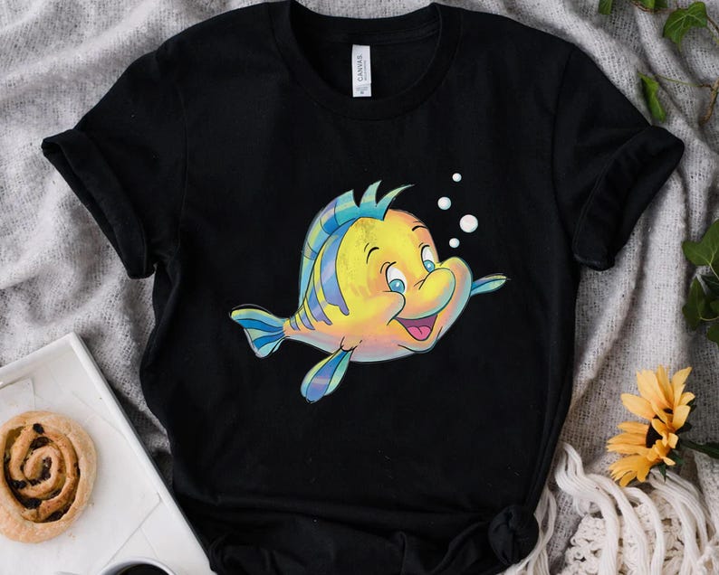 K&ouml;nnte beinhalten: Schwarzes T-Shirt mit einer Cartoon-Illustration eines gelb-blauen Fisches mit l&auml;chelndem Gesichtsausdruck. Der Fisch hat blaue Flossen und ist von wei&szlig;en Blasen umgeben. Das Shirt ist aus weichem Material.