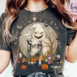 May include: Dark gray t-shirt featuring a Halloween-themed graphic. The design includes Jack Skellington, Sally, and Oogie Boogie in front of a full moon, with bats and pumpkins. The shirt has a vintage, worn look.