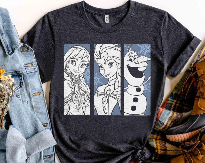 May include: A dark heather gray short-sleeve t-shirt featuring a graphic print of three vertical panels. The panels display line art illustrations of Anna, Elsa, and Olaf from Frozen, set against a light blue background with snowflake accents.