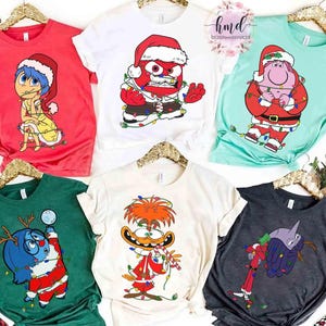 May include: A collection of Christmas-themed t-shirts featuring cartoon characters. The shirts are in various colors, including red, white, green, and teal. Each shirt has a different character wearing a Santa hat and Christmas lights.