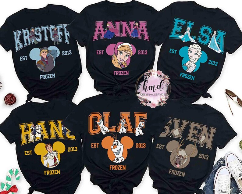 May include: Black t-shirts featuring characters from the movie Frozen. Each shirt has a character's name in a collegiate font, the year 2013, and the word "FROZEN". Characters include Kristoff, Anna, Elsa, Hans, Olaf, and Sven.