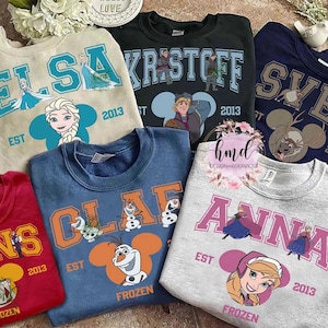 May include: A collection of crewneck sweatshirts featuring characters from the movie Frozen. Each sweatshirt displays a character's name, the year 2013, and a character illustration. Colors include red, blue, gray, and green.
