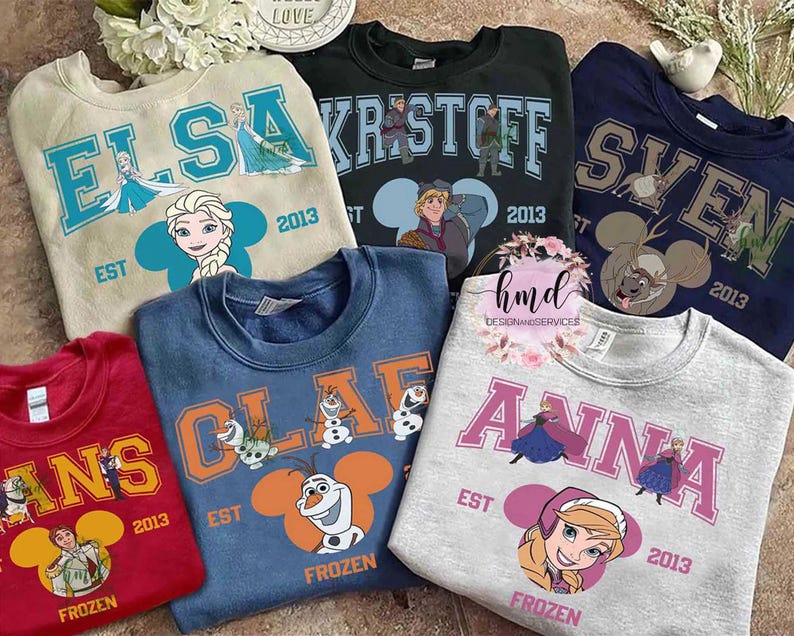 May include: A collection of crewneck sweatshirts featuring characters from the movie Frozen. Each sweatshirt displays a character's name, the year 2013, and a character illustration. Colors include red, blue, gray, and green.