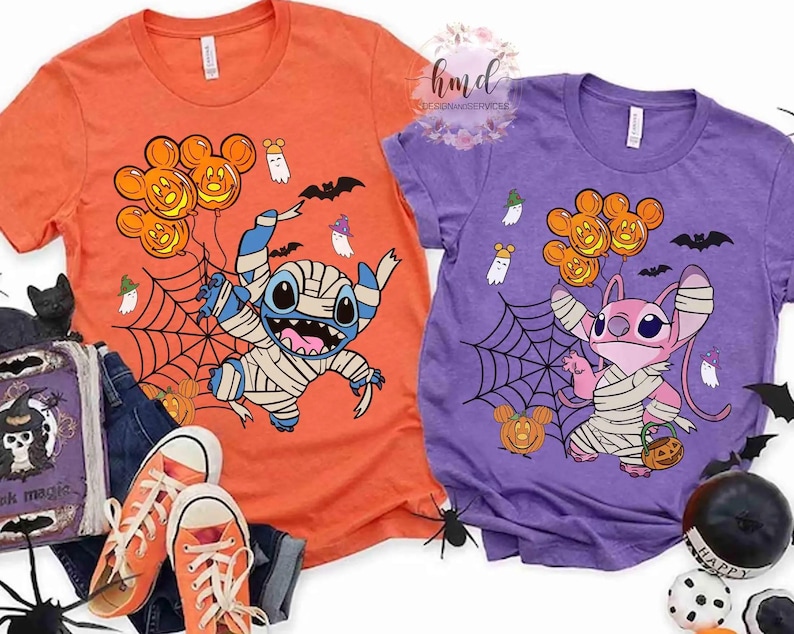 Op de afbeelding: Twee Halloween-t-shirts. E&eacute;n is oranje met een mummie-achtig Stitch-personage dat Mickey Mouse pompoenballonnen vasthoudt. De andere is paars met een roze Angel-personage dat Mickey Mouse pompoenballonnen vasthoudt. Beide shirts hebben spinnenwebben, geesten en vleermuizen.